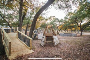 Explore the park's playground, featuring a wooden play structure with a ladder and swing set, surrounded by trees and a wooden deck.