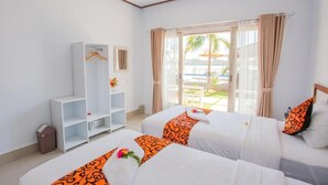 Quarto de hotel com duas camas, um guarda-roupa e vista para a piscina e palmeiras.