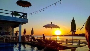 Área da piscina com guarda-sóis, espreguiçadeiras e vista para o pôr do sol.