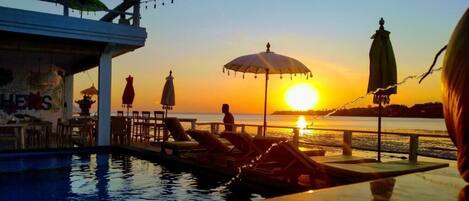 A poolside area with umbrellas, lounge chairs, and a sunset view.