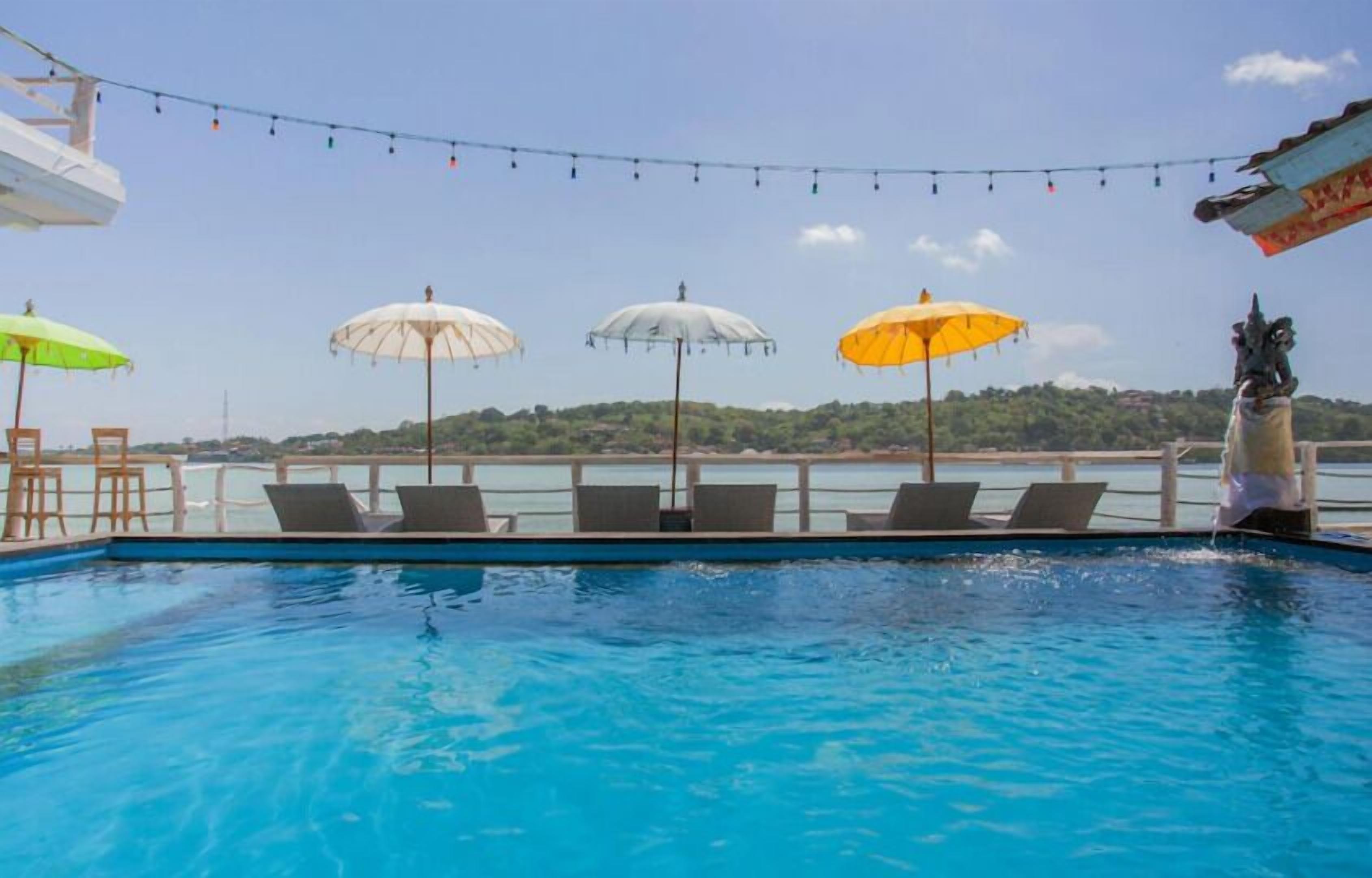 A poolside area with lounge chairs and umbrellas, a statue, and a view of a distant shoreline.