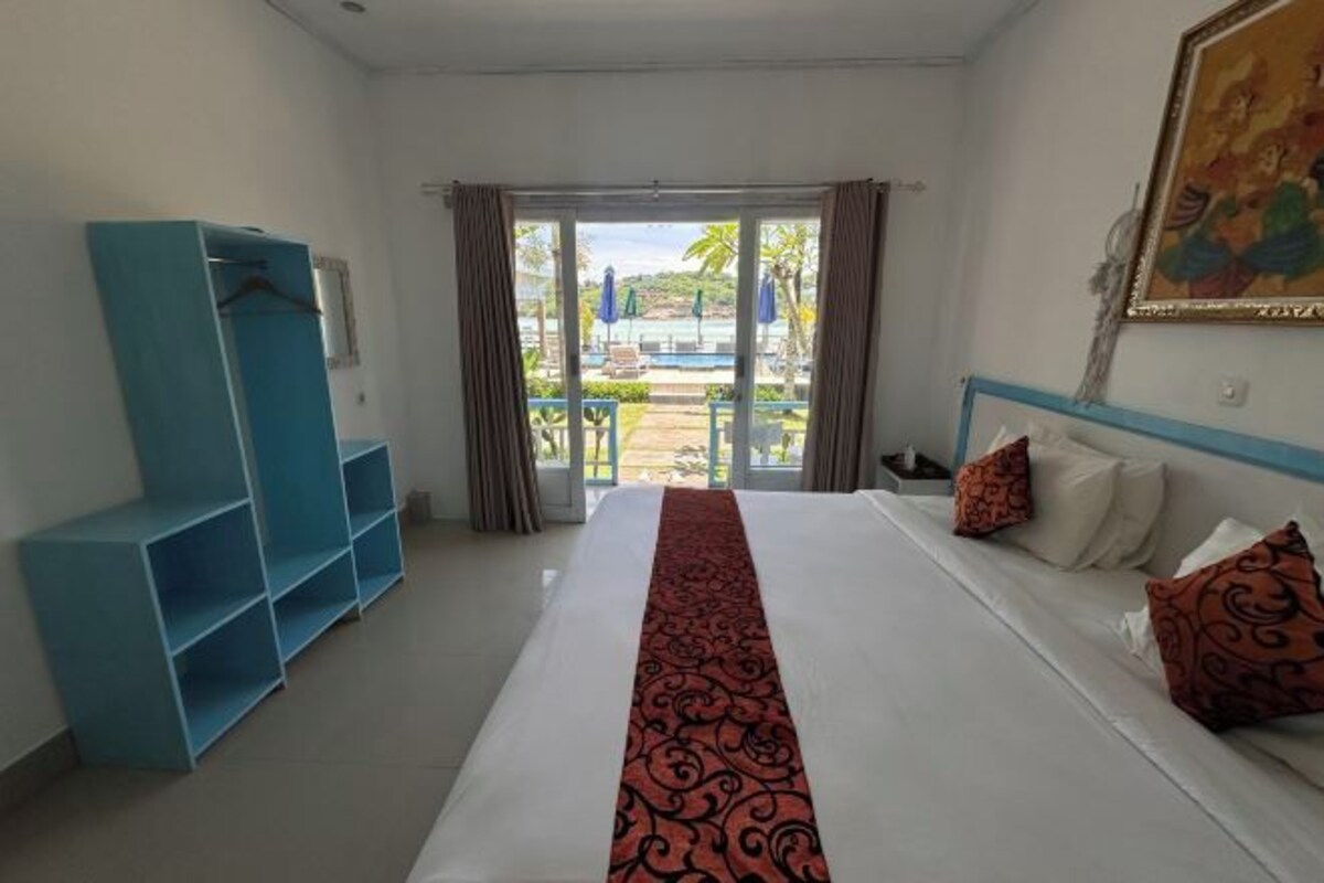 Habitación de hotel con una cama, un estante azul, y vista a una piscina y palmeras a través de la ventana.