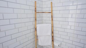 Canto de um banheiro com paredes revestidas de azulejos brancos, um porta-toalhas de bambu e uma toalha branca pendurada nele.