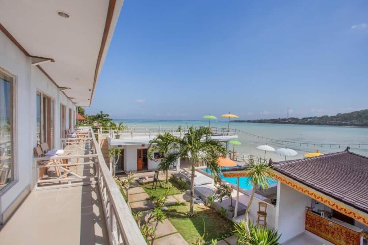 A balcony with a view of the sea, a pool, and outdoor seating.