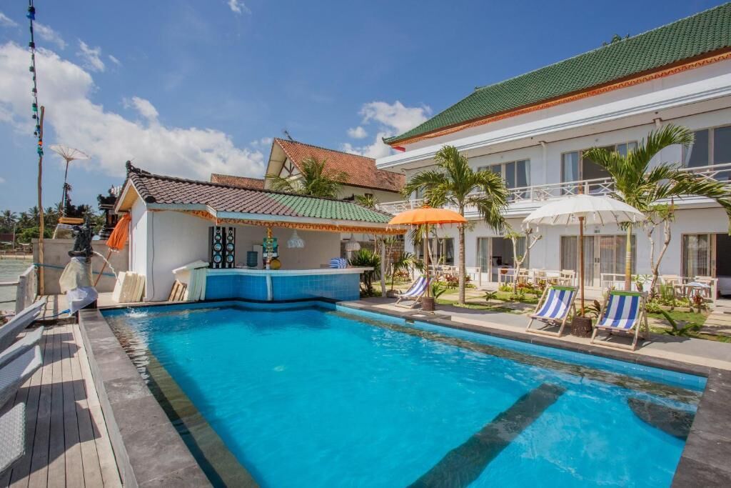 A swimming pool with lounge chairs and umbrellas, a bar area, and a building with a tiled roof.