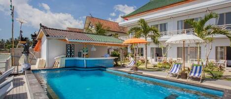 A swimming pool with lounge chairs and umbrellas, a bar area, and a building with a tiled roof.