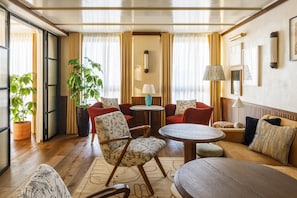 Ein gut beleuchteter Raum mit Holzboden, roten Sofas, einem runden Tisch und einer großen Topfpflanze.