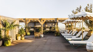 En takterrass med träpergola, solstolar och krukväxter.