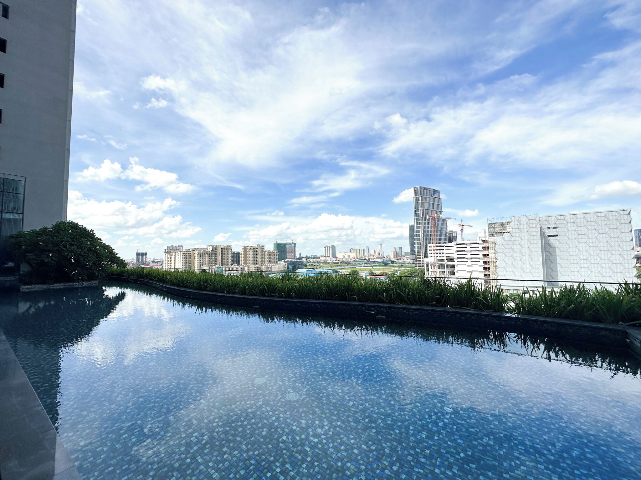 Une piscine sur le toit offrant une vue sur le paysage urbain, entourée de verdure et de bâtiments modernes.