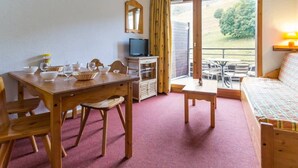 A cozy room with a wooden dining table, chairs, a sofa, a television, and a balcony with a view of greenery. - Duplex 3-room, 8 pers, balcony, near slopes (Le Corbier)