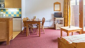 A cozy room with a wooden dining table, chairs, a TV, and a small cabinet. - Duplex 3-room, 8 pers, balcony, near slopes (Le Corbier)