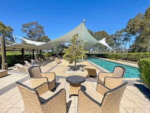 Un espace aménagé au bord de la piscine, avec des meubles en osier et un auvent.