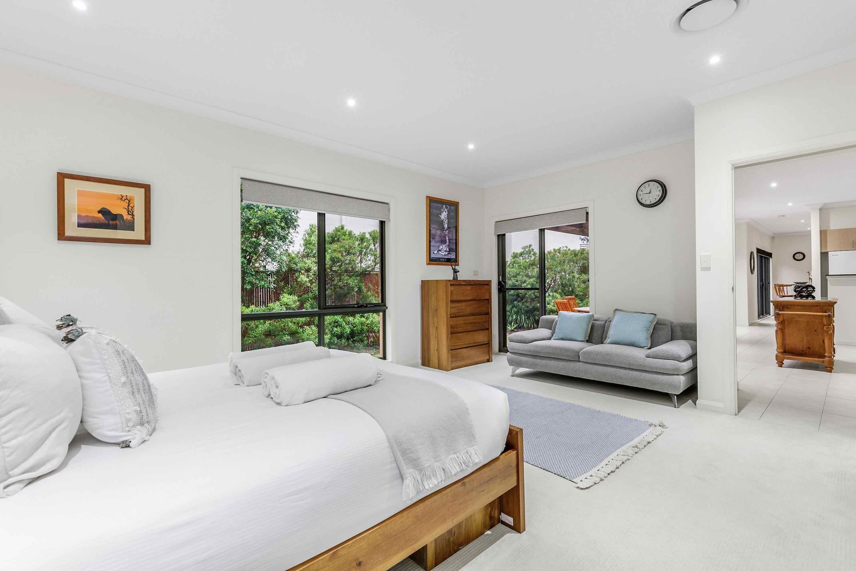 A modern bedroom with a large bed, a grey sofa, and a wooden wardrobe.