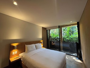 A modern hotel room with a large bed, a nightstand, a wall-mounted lamp, and a sliding glass door leading to a balcony with greenery. - w* | Alluring 2BR with Balcony in Condesa (Ciudad de México)