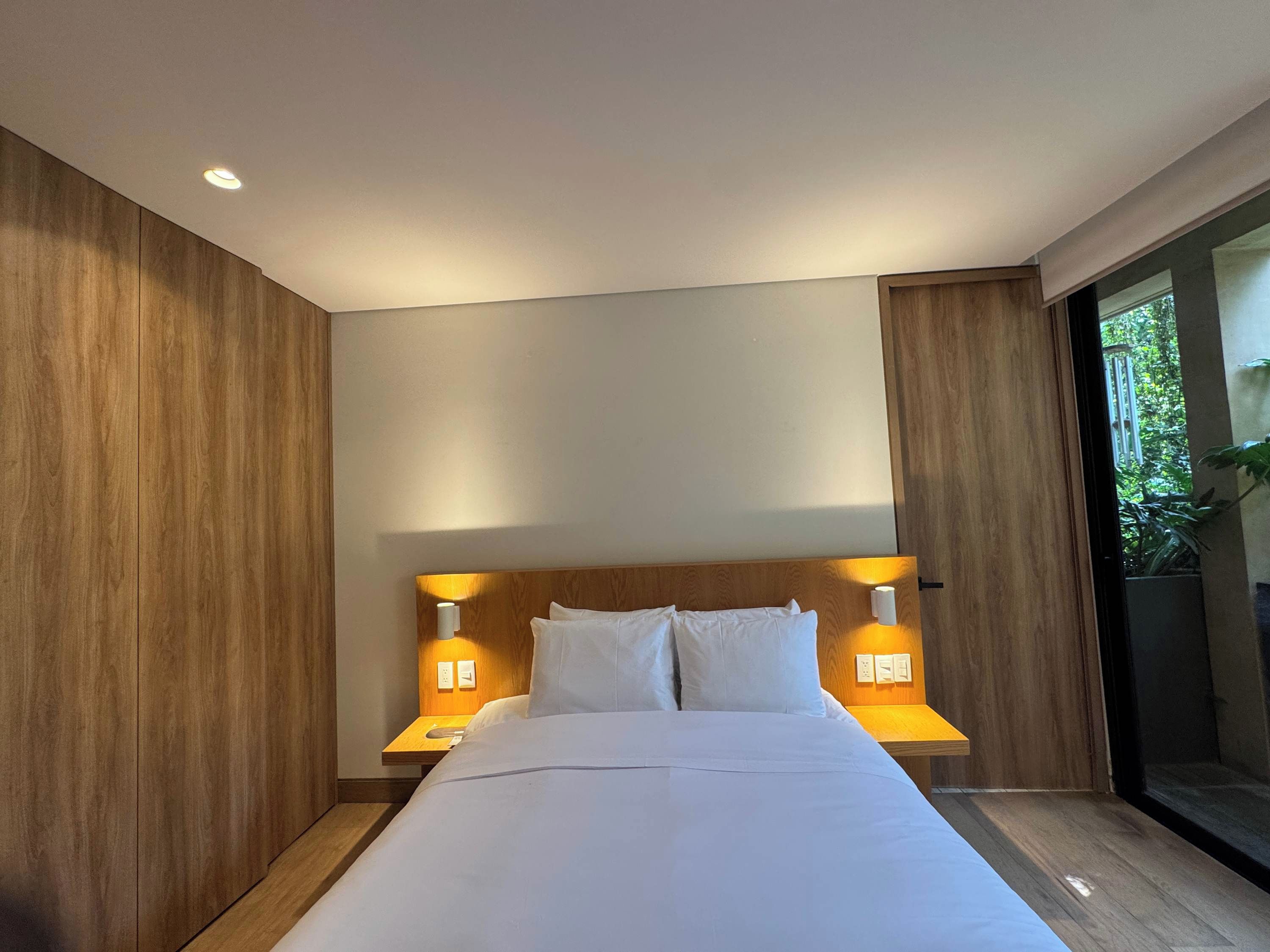 Ein modernes Hotelzimmer mit einem großen Bett, einem Holz-Kopfteil und zwei Nachttischlampen.