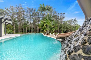 A swimming pool with clear blue water, surrounded by trees and a stone wall. - The Noosa Ranch - Where Nature meets Luxury (Tinbeerwah)