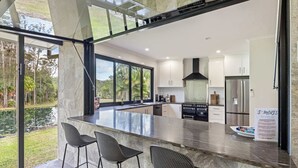 A modern kitchen with a large island, bar stools, and a view of a garden. - The Noosa Ranch - Where Nature meets Luxury (Tinbeerwah)