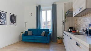 A modern living room with a blue sofa, a small side table with a plant, and a view through a glass door to the outside. - The Best Rent - Contemporary two bedroom flat in Porta Romana (Milano)