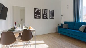 A modern living room with a dining area, a blue sofa, and three abstract art pieces on the wall. - The Best Rent - Contemporary two bedroom flat in Porta Romana (Milano)