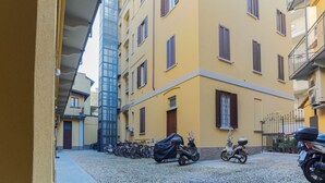 A courtyard with a row of parked bicycles and scooters, a building with yellow walls and brown shutters, and a modern glass structure in the background. - The Best Rent - Contemporary two bedroom flat in Porta Romana (Milano)