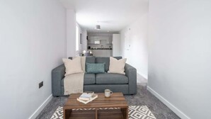 A modern living room with a grey sofa, a wooden coffee table, and a patterned rug. - Contemporary 1 Bedroom Liverpool Apartment (Liverpool)