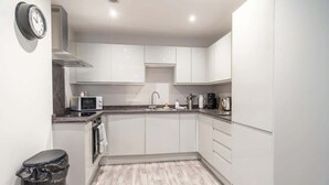 A modern kitchen with white cabinets, a microwave, a coffee maker, and a trash bin. - Contemporary 1 Bedroom Liverpool Apartment (Liverpool)