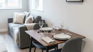 A dining area with a wooden table set for four, a grey sofa, and a framed abstract artwork on the wall. - Contemporary 1 Bedroom Liverpool Apartment (Liverpool)