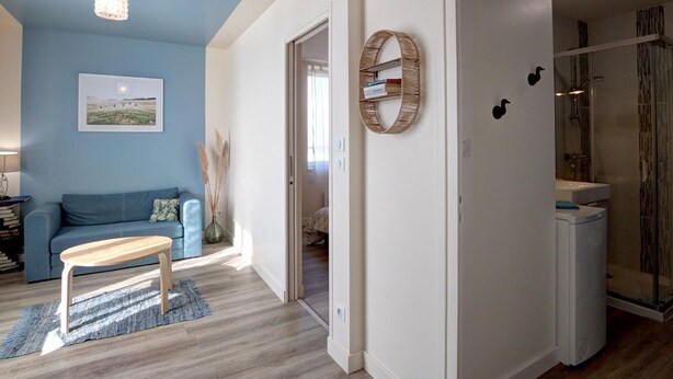 Ein modernes Wohnzimmer mit blauer Akzentwand, einem Holztisch, einem blauen Sofa und einer hängenden Leuchte.