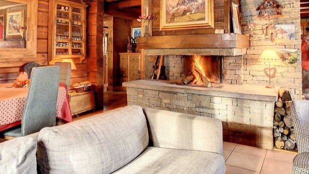 A cozy log cabin interior with a fireplace, wooden furniture, and a bookshelf.