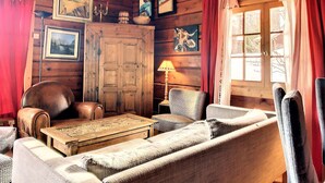 A cozy log cabin interior with a wooden dining table, leather armchairs, a sofa, and a fireplace.