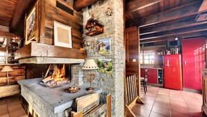 A rustic kitchen with a stone wall, wooden beams, a fireplace, and a red refrigerator.