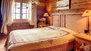A cozy wooden cabin bedroom with a large bed, a nightstand, a lamp, and a window with curtains.