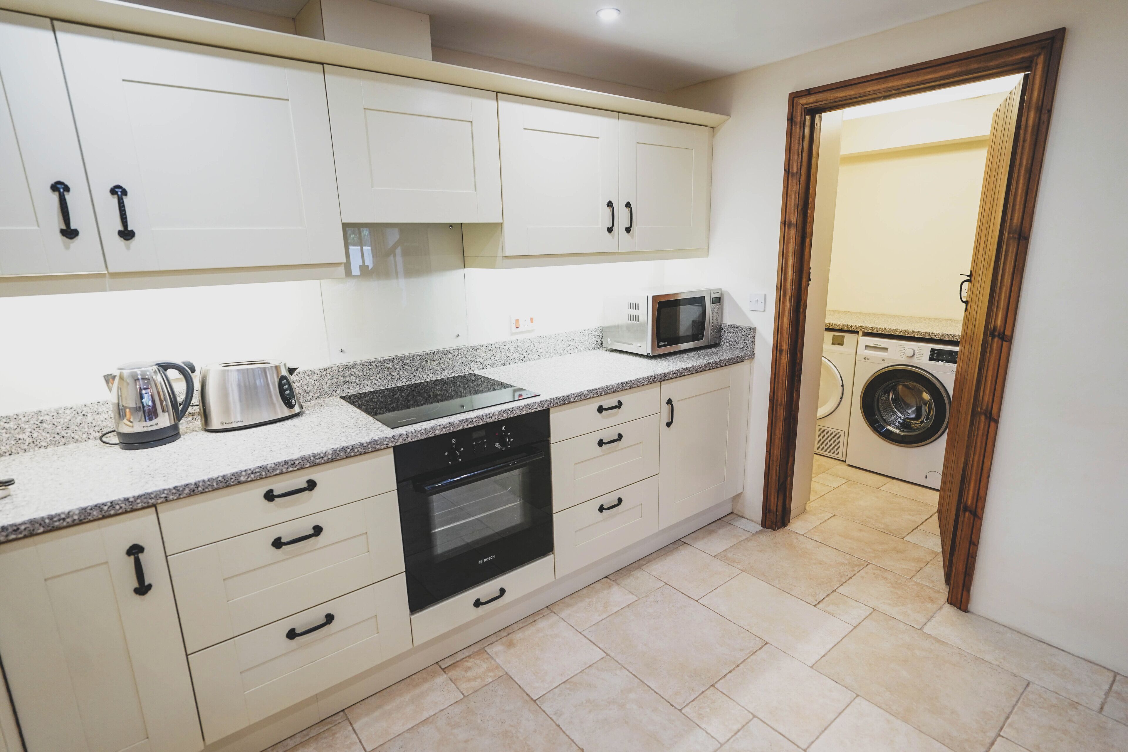 A kitchen with white cabinets, a microwave, a kettle, and an oven.