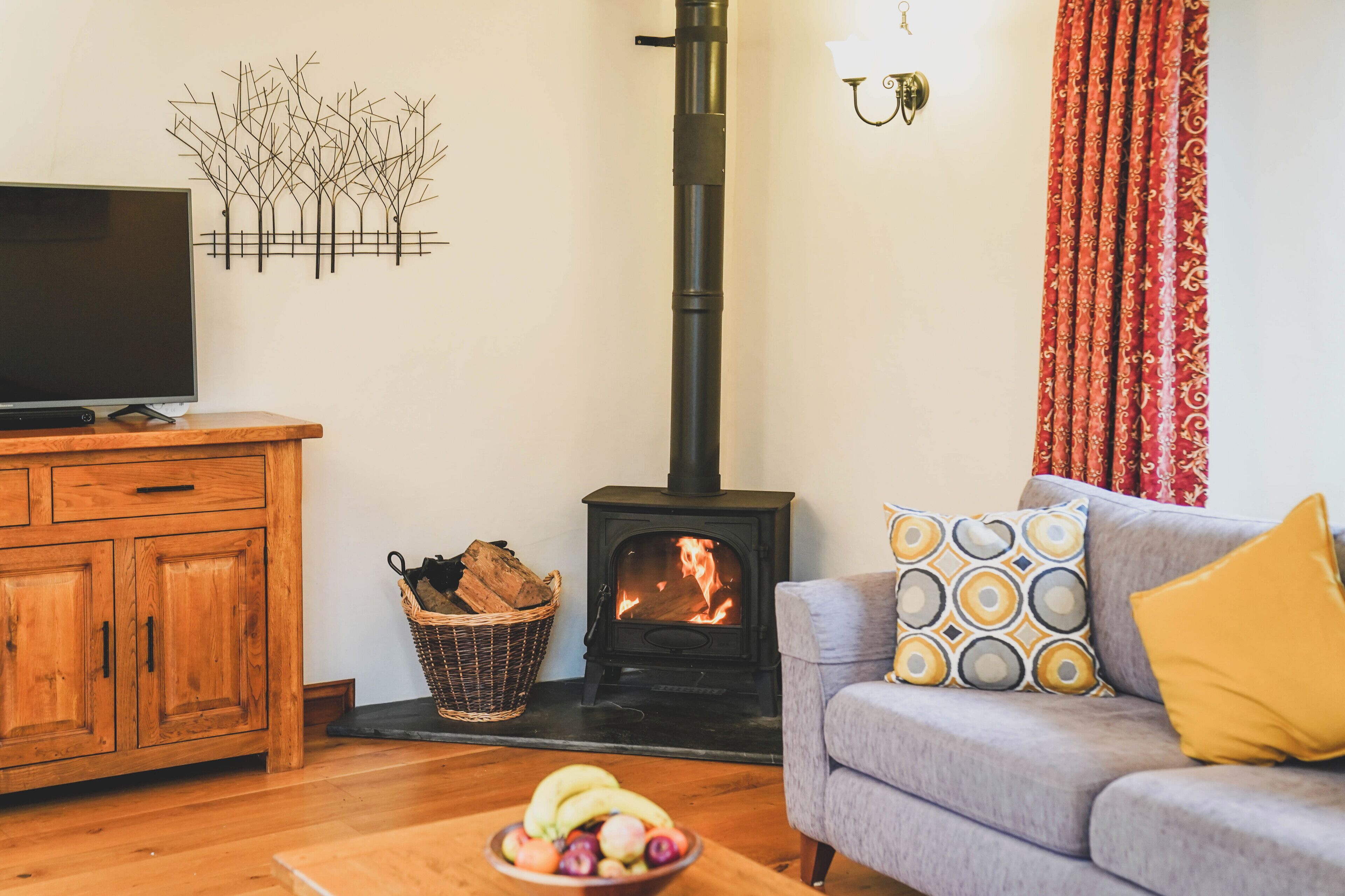 A living room with a television, a fireplace, a sofa with patterned cushions, and a fruit bowl on the floor.