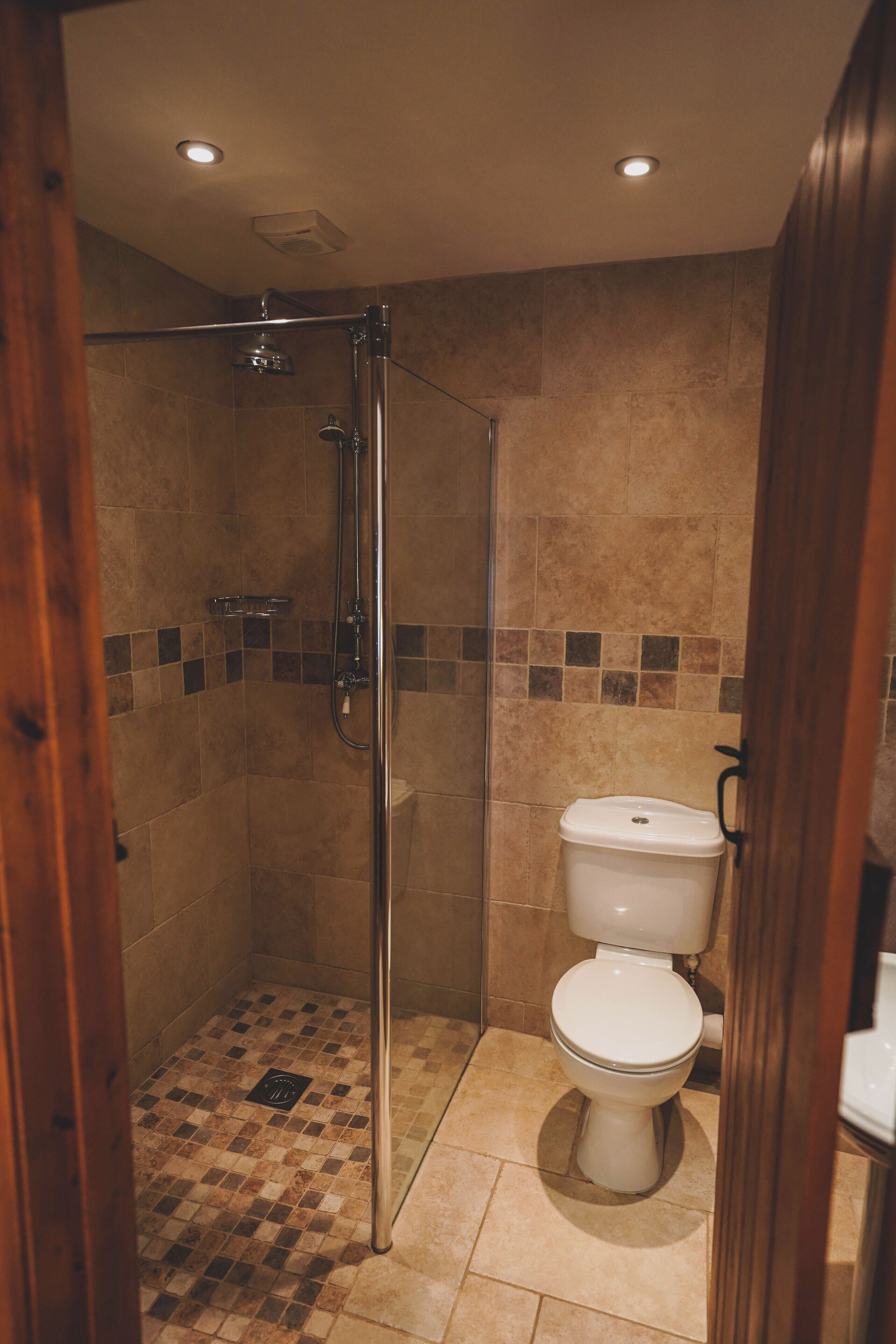 A shower with a glass door, a toilet, and a tiled floor.