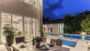 A dining area with a poolside view, featuring a table set with plates, glasses, and a bottle.