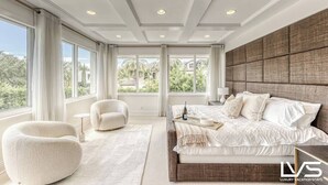 A modern bedroom with a large bed, a comfortable chair, and a view of the outdoors.