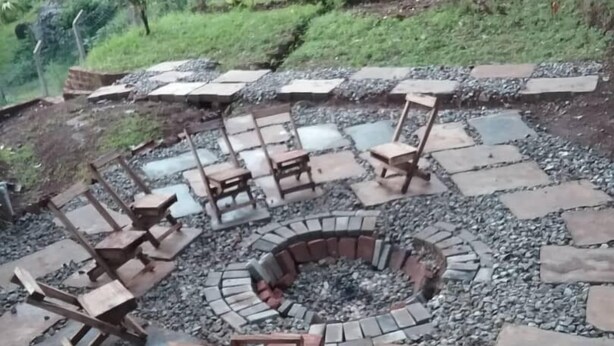 Een rond zitgedeelte buiten, met stenen vloeren en houten stoelen, omgeven door een lage stenen muur.