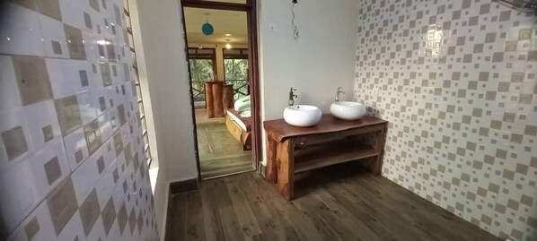 A bathroom with a wooden vanity, two sinks, and a view of a balcony with a bed. -  Wanale Falls Lodge (Mbale)