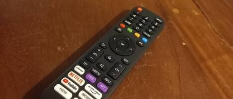 A remote control on a wooden table with a bed in the background.