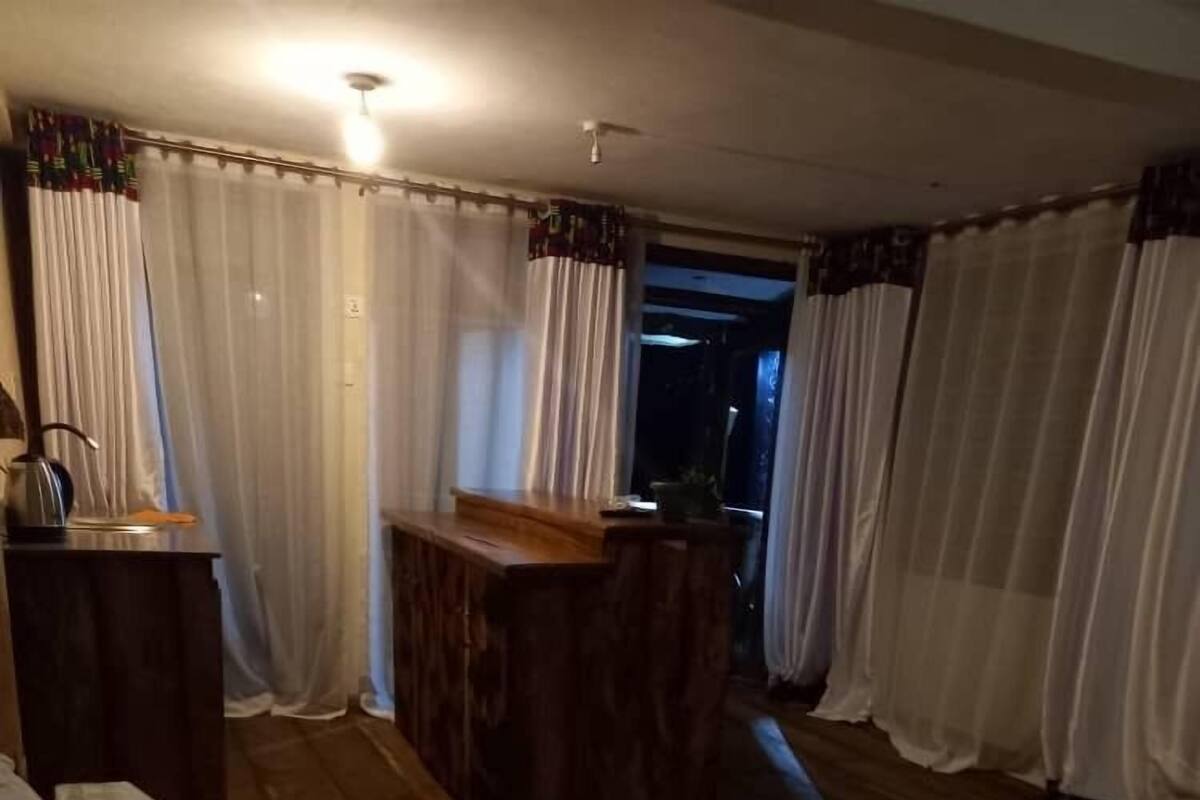 A hotel room with a bed, a wooden desk, and a view through a window with curtains.