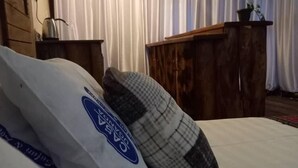 Een slaapkamer met een bed, kussens, een houten dressoir en een gordijn.