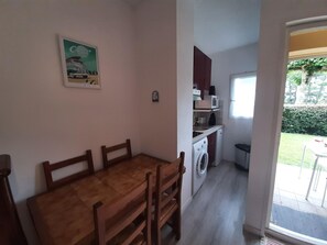 A compact kitchen with a washing machine, a microwave, and a small dining area with a wooden table and chairs. - Cozy Apartment in Capbreton - Port View, Sleeps 4, Terrace, 500m from Beach (Capbreton)