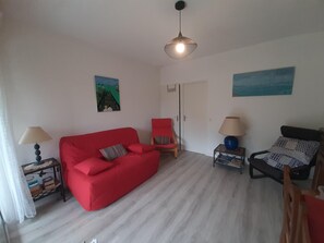 A living room with a red sofa, a red armchair, a blue lamp, and a black chair. - Cozy Apartment in Capbreton - Port View, Sleeps 4, Terrace, 500m from Beach (Capbreton)