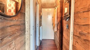 A wooden hallway with a mirror, a door, and a wall-mounted light fixture.