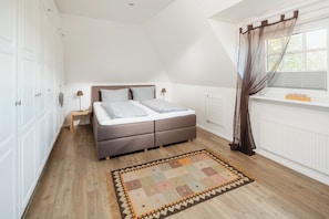 Une chambre à coucher avec un lit, des tables de chevet, une fenêtre avec des rideaux et un radiateur.