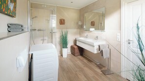 A modern bathroom with a glass shower enclosure, a white bathtub, a sink with a mirror, and a potted plant. - // Liebeney - Möwennest // (Norderney)