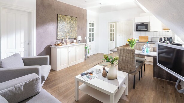 A modern living room with a sofa, coffee table, and a dining area with a wicker chair. - // Liebeney - Möwennest // (Norderney)