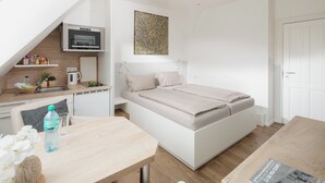 A compact bedroom with a bed, a small kitchenette, a dining area, and a bathroom. - LIEBENEY - BEACH CHAIR // (Norderney)