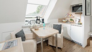 A modern kitchen with a microwave, coffee maker, and a small dining area with a table and chairs. - LIEBENEY - BEACH CHAIR // (Norderney)
